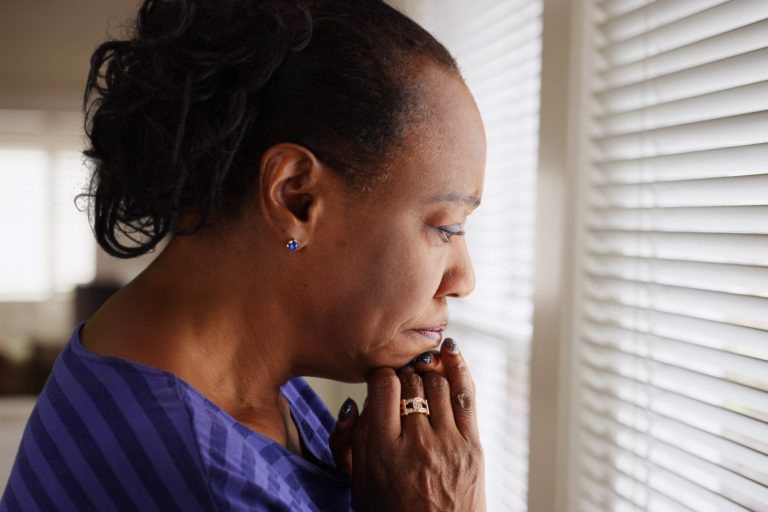 An older black woman mournfully looks out her window An older black woman mournfully looks out her window
