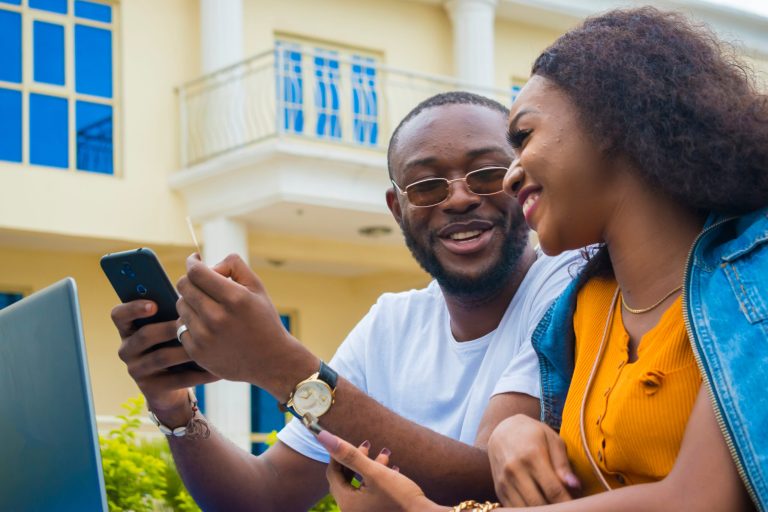 two african couple having a nice time in a park feeling happy ab two african couple having a nice time in a park feeling happy about the transaction they did on their cellphone,telephone, smartphone using a credit card.