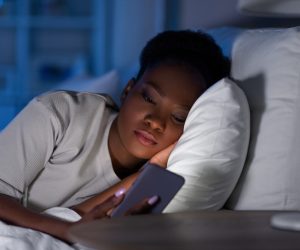 african woman with smartphone in bed at night How to stop early morning urgent phone calls from family
