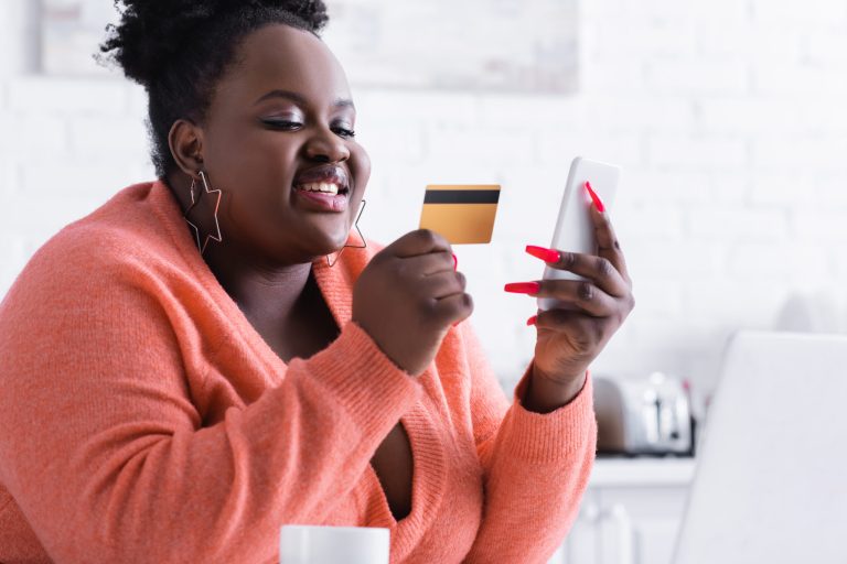 smiling african american plus size woman holding credit card and smiling african american plus size woman holding credit card and mobile phone